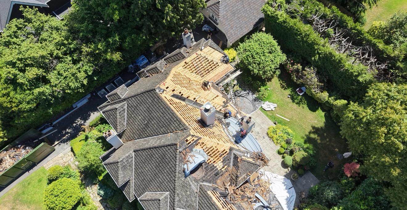 Crew replacing roof decking mid-tear-off, with old cedar stripped and new plywood going down over the rafters